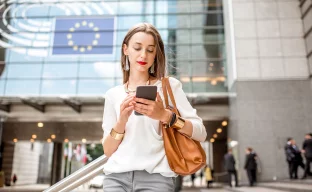 Junge Geschäftsfrau mit Telefon in der Nähe des Parlamentsgebäudes der Europäischen Union in Brüssel