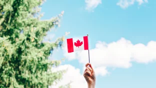 Nahaufnahme einer weiblichen Hand, die vor blauem Himmel eine kanadische Flagge schwenkt Nahaufnahme einer weiblichen Hand, die vor blauem Himmel eine kanadische Flagge schwenkt