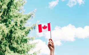 Nahaufnahme einer weiblichen Hand, die vor blauem Himmel eine kanadische Flagge schwenkt