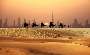 Mann und Kamele in einer Karawane mit Touristen auf Sanddünen in der arabischen Wüste
